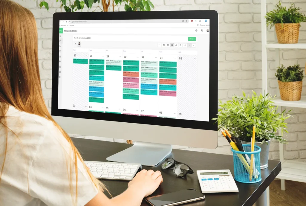 Tela de computador mostrando uma agenda digital organizada, com profissional da saúde analisando os horários e automações de lembretes.