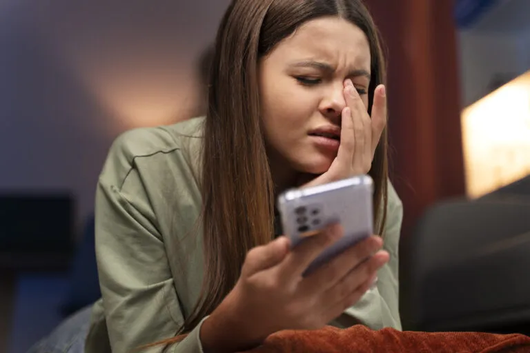Jovem mulher com expressão de frustração ao olhar para o celular, representando uma paciente insatisfeita com a demora no atendimento da clínica via WhatsApp e o risco de perda de agendamento.