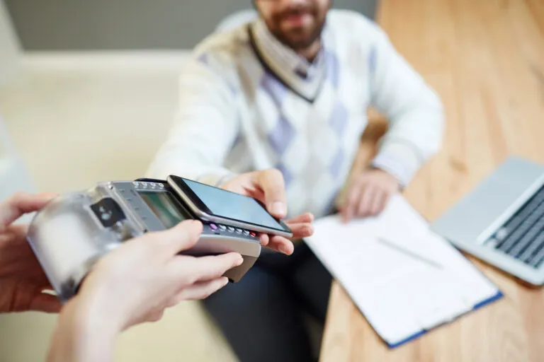 Paciente realizando um pagamento digital (PIX ou smartphone) na recepção da clínica odontológica, um processo facilitado pela automação de cobrança da Secretária IA.