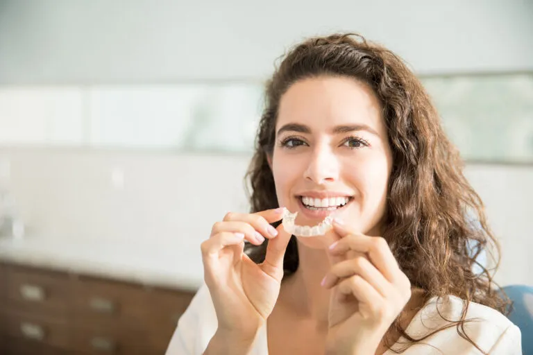Paciente de ortodontia sorrindo e segurando um alinhador invisível, simbolizando a gestão moderna e digital que a Secretária IA oferece para clínicas de ortodontia.