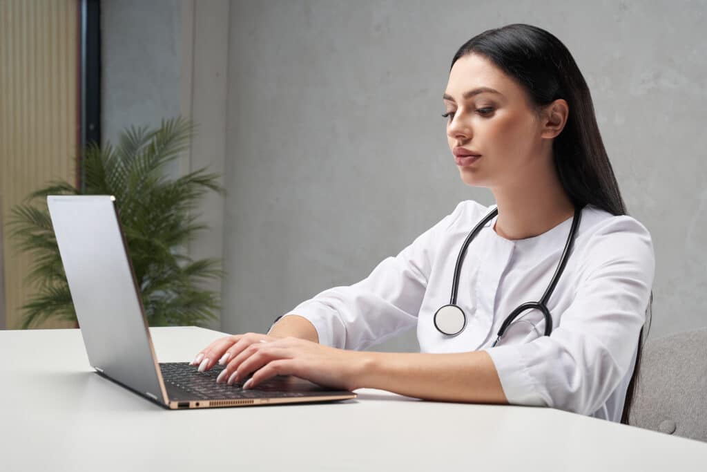 Médica usando notebook em consultório, representando IA com memória de longo prazo para atendimento de pacientes em clínicas.